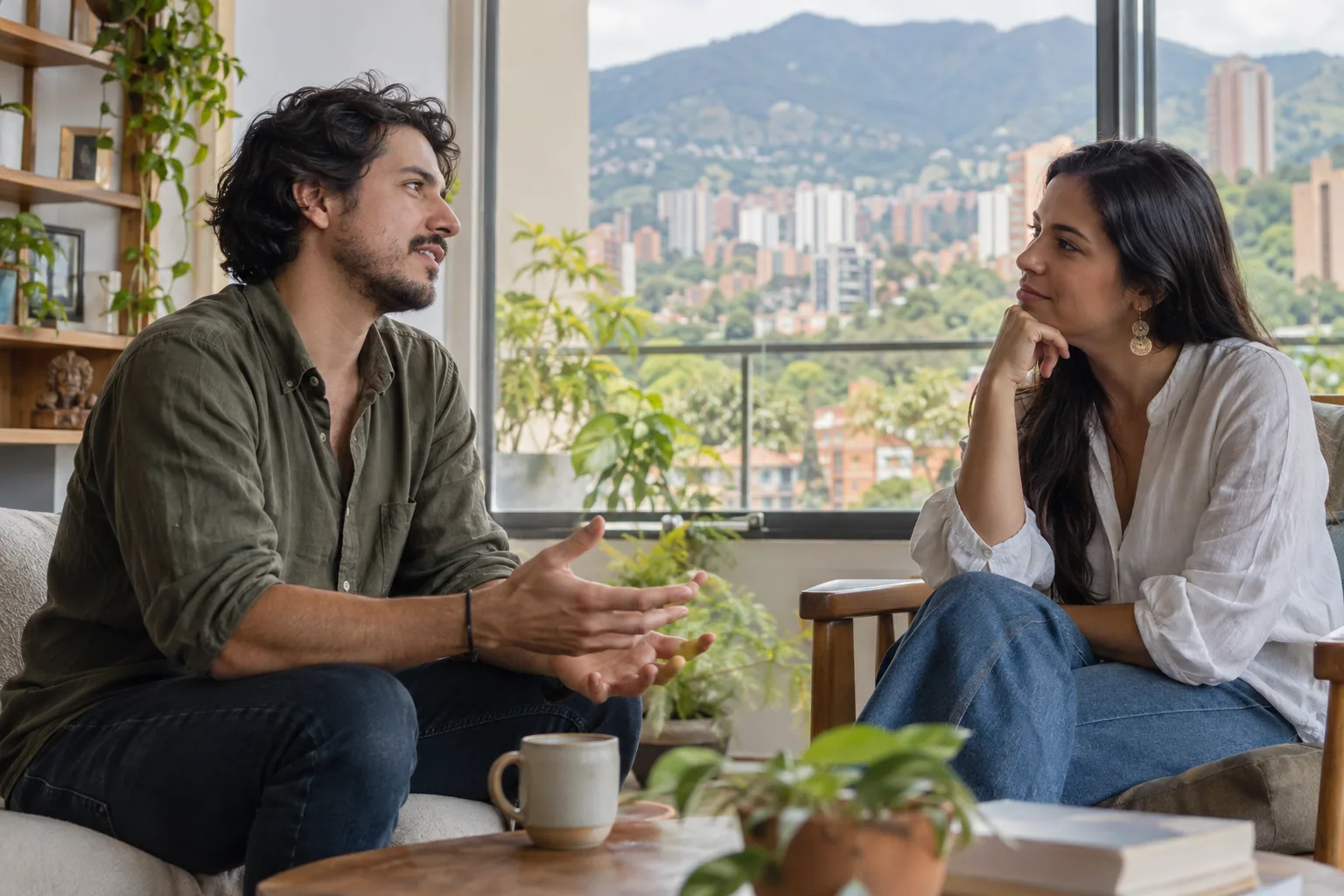 Dos personas adultas conversan en un espacio luminoso con vista a la ciudad.